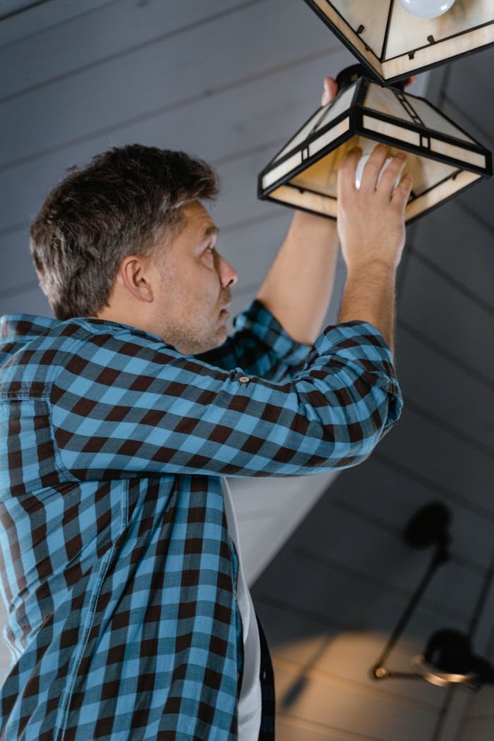 Man in a plaid shirt installs a lightbulb in a stylish interior setting.